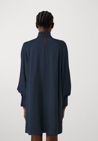 Laivasil tilalted dressi, yüksek boyun, düğmeli manşetlere sahip uzun kollar ve arka kısmında anahtar deliği detayı. Pürüzsüz doku ve bol kesim.