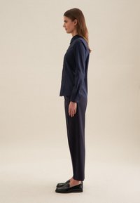 Marineblauwe overhemd met gestructureerde kraag, gecombineerd met slim-fit donkere broek en zwarte instappers, gepresenteerd tegen een neutrale achtergrond.