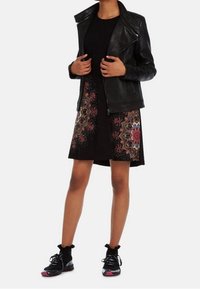 Svart läderbikerjacka över en kort svart klänning med flerfärgade blommönster, parat med svarta sneakers med rosa detaljer.