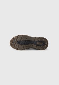 Suela de zapato Skechers con un diseño texturizado y resistente en goma negra y marrón, con patrones de profundidad para tracción.