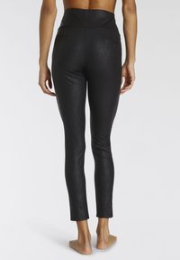 Leggings neri caratterizzati da un motivo a spina di pesce e una vita alta con due tasche posteriori. Il materiale ha una leggera lucentezza ed è aderente.