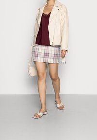 Beige leren bikerjack, bordeauxkleurige top met kantafwerking, geruite minirok in wit, blauw en roze, gecombineerd met naakte platte sandalen.