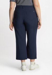 Pantaloni cropped blu navy con una texture liscia e cintura elastica. Presentano due tasche posteriori con dettagli dorati. Indossati con sneakers bianche.
