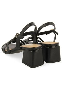 Sandales noires à talons avec des lanières en cuir croisées et un talon carré. Elles disposent d'une semelle intérieure lisse et d'une sangle de cheville ajustable.