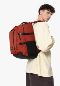 Mochila roja y negra hecha de tela duradera, con correas ajustables, múltiples compartimentos y un acabado texturado.