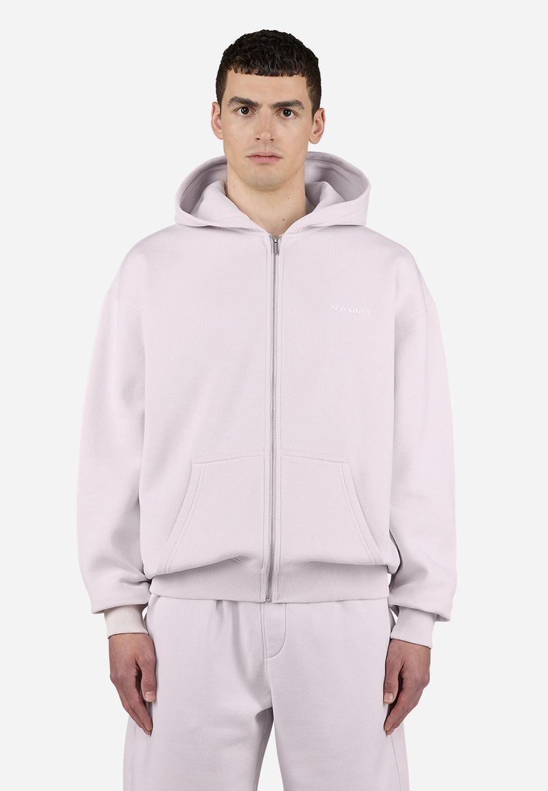 Sudadera con cremallera de color rosa claro, hecha de un tejido suave, que presenta una cremallera frontal, dos bolsillos y puños y dobladillo acanalados. Logo de texto en el pecho.