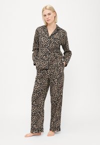 Pysjamasett med leopardmønster, laget av myk stoff, med en knapp-oppe topp med lomme og løstsittende bukser. Farger: beige og mørkebrun.
