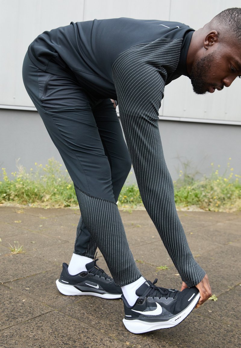 Schwarzes Sportoutfit mit gestreiften Akzenten, taillierter Passform, feuchtigkeitsableitendem Material und schwarzen Nike-Laufschuhen mit weißer Sohle.