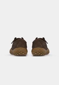Zapatillas de ante marrón con un diseño redondeado, que cuentan con suelas de goma texturizadas y dos bucles en la parte trasera para facilitar su uso.