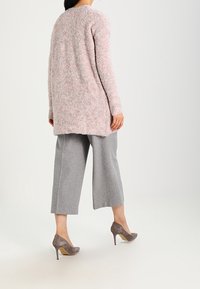Cardigan lungo, rosa, con texture, realizzato in morbido tessuto a maglia, abbinato a pantaloni grigi a gamba larga e scarpe con tacco grigie.