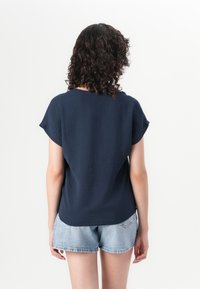 Navyblaues Kurzarmoberteil aus strukturiertem Stoff. Rundhalsausschnitt und lockere Passform, kombiniert mit hellblauen Denim-Shorts. Minimalistisches Design.