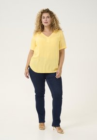 Haut jaune à manches courtes avec un col en V et une finition texturée, associé à un jean skinny bleu foncé et des talons jaunes à brides.