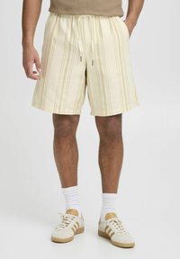 Pantalones cortos a rayas de color amarillo claro con cintura elástica y cordón. Presenta bolsillos laterales y un ajuste relajado, fabricados con un tejido texturizado.