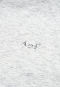 Sivá bavlnená tričko s textúrovaným povrchom a vyšívaným logom "A&F" v striebornej farbe na ľavej strane. Pohodlný, neformálny dizajn.