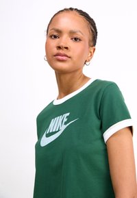 Green cotton t-shirt with white ribbed collar and cuffs, featuring a large white Nike logo printed on the front.