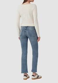 Striped cream long-sleeve shirt, blue jeans with a straight leg, and lightweight sneakers with black accents and gum soles.