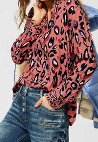 Blouse rose à manches longues avec imprimé léopard noir et bleu ; associée à un jean en denim bleu clair avec poche zippée et détail de bouton.