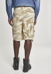 Beige camouflage cargo shorts med sidofickor, i bomullsmaterial, utrustade med bälteslingor, i kombination med svarta ankelboots.