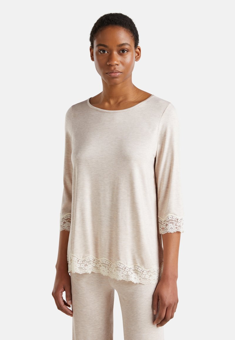 Top de manga larga color beige claro con cuello redondo y borde de encaje en las mangas y el dobladillo. Textura suave, ajuste ligeramente holgado.