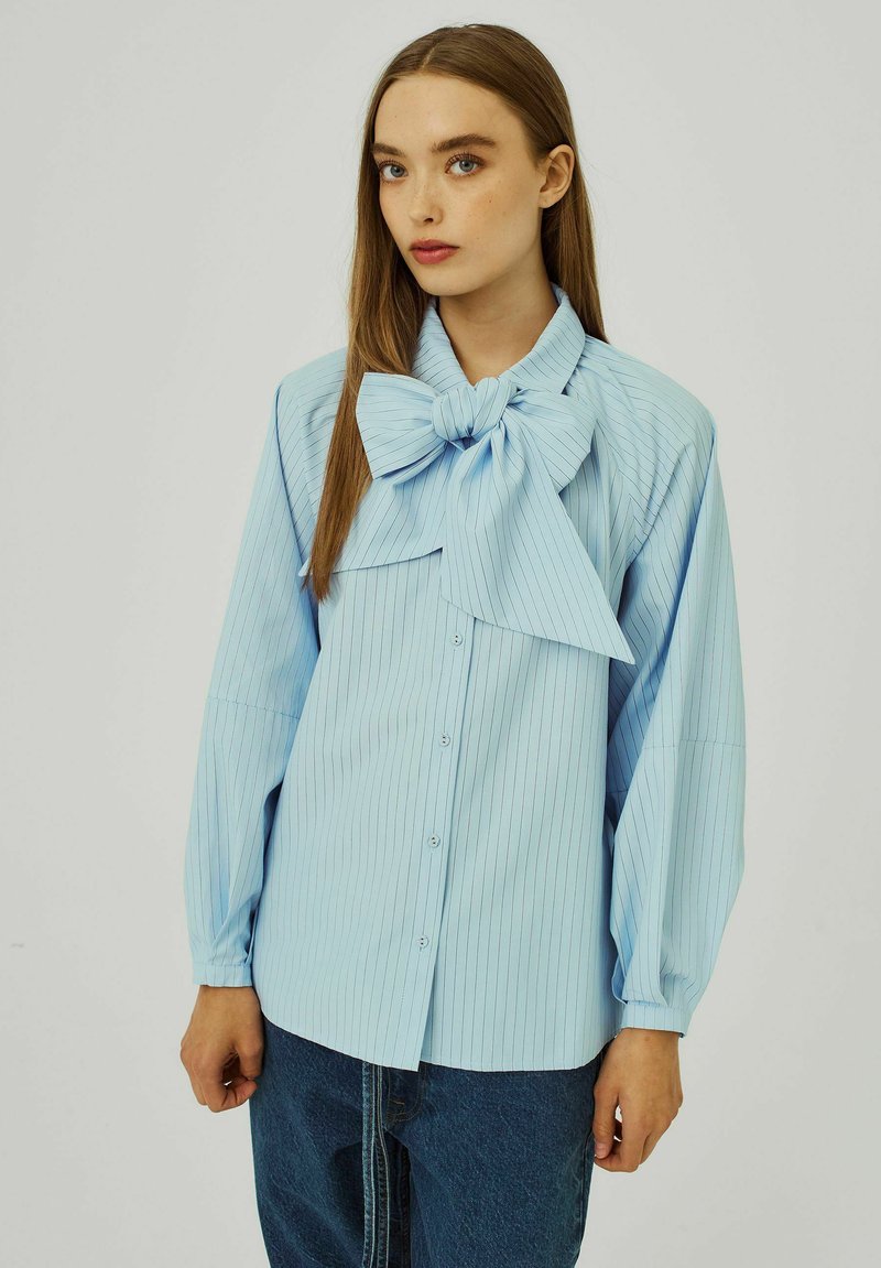 Lichtblauwe gestreepte blouse met een grote strikboord, lange mouwen en een knoopsluiting. Gemaakt van soepele stof met een relaxte pasvorm.