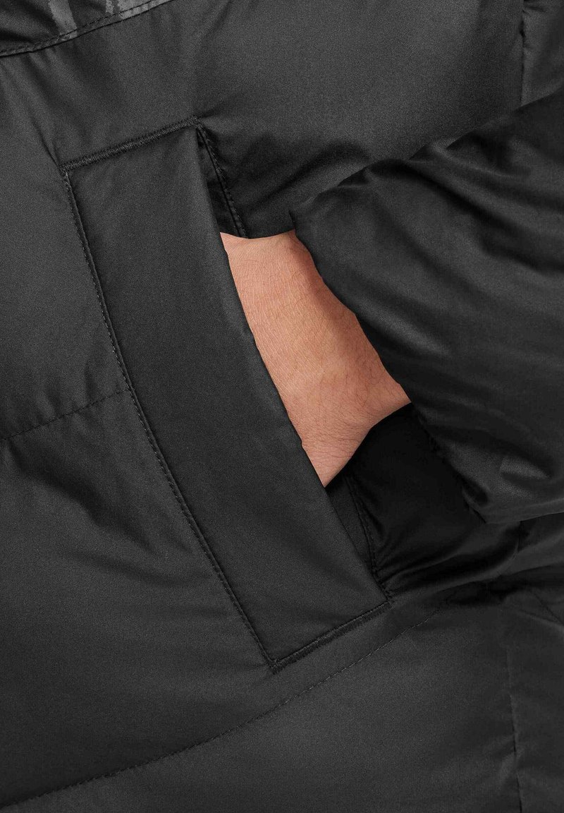 Tejido de chaqueta acolchada negra con un bolsillo lateral oculto. Textura suave con costuras cosidas y un diseño minimalista.