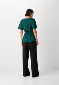 Top peplum color teal con maniche corte, vita aderente e un sottile motivo testurizzato, abbinato a pantaloni neri a gamba larga con vita alta.