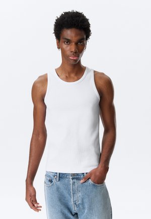 Hvit bomullstopp med ribbet tekstur, rund halslinje og brede skulderstropper, sammen med lyseblå denimjeans.