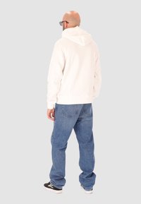 Felpa bianca con un taglio rilassato e cappuccio con coulisse, abbinata a jeans baggy azzurri. L'outfit presenta polsini a coste e una texture morbida.