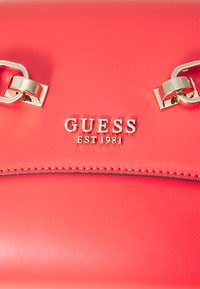 Coral leather handbag with silver metal hardware. Features embossed "GUESS EST 1981" logo and stitched detail along the edges.