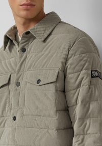 Gequilted taupe shirtjacket van ribstof, met zwarte knopen, twee borstzakken en een gestikte designt patroon.