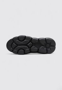 Semelle de chaussure de sport noire avec caoutchouc texturé, motifs de traction multidirectionnels et indentations circulaires pour une adhérence et une stabilité optimales.