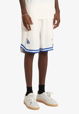 Person trägt weiße Los Angeles Dodgers Basketballshorts mit blauer Umrandung, schwarze Socken und weiße Sneakers mit Gummisohlen.