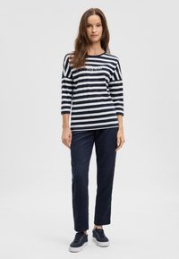 Navy and white striped long-sleeve shirt with round neckline, paired with dark navy pants and navy sneakers. Simple text logo on shirt.