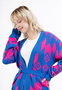 Modrý kardigán s jemnými ružovými geometrickými vzormi, s výstrihom do V, dlhými rukávmi a zodpovedajúcim opaskom, vyrobený z pleteného materiálu.