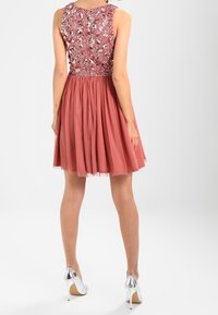 Bezrukávové šaty do kolen se růžovou plisovanou sukní a korzetem zdobeným flitry, doplněné kovovými vysokými podpatky.