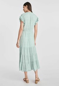 Maxi sukienka w miętowym kolorze z kwiecistym wzorem, falbaniastymi rękawami, elastycznym pasem i warstwowym dołem. Nosi z beżowymi sandałami na paski.