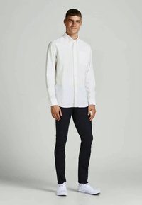 Balta garām piedurknēm krekls ar pogājamām malām, saskaņots ar tumšām šaurām biksēm un baltām sporta apaviem. Vienkārša dizaina, viegla auduma.