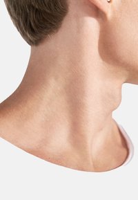 Nära bild av en hals med slät, ljus hud, kort brunt hår, som visar subtila konturer och en litenörhänge i vänster öra.