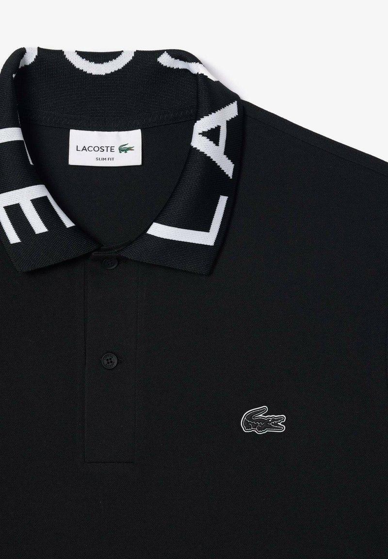 Schwarzes Slim-Fit-Polo-Shirt aus strukturiertem Stoff mit einem kontrastierenden weißen Logo am Kragen und einem kleinen gestickten Krokodil-Emblem.