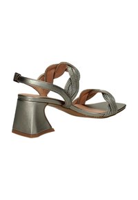 Sandalias de tacón plateadas metálicas con correas trenzadas, diseño de punta abierta y tacón grueso. Textura suave, correa ajustable en el tobillo.