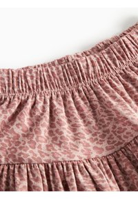 Sammentrekket stoff i en myk rosa tone med et subtilt leopardmønster. Teksturen viser folder ved livsnivået.