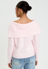 Pull rose à épaules dénudées avec un col et des poignets côtelés, en tissu doux et texturé avec une coupe ajustée.