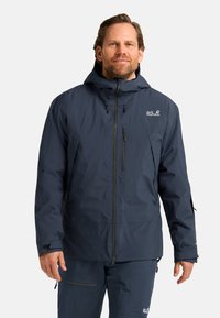 Giacca impermeabile navy con cappuccio, zip anteriore e numerose tasche con cerniera. Presenta polsini elastici e un logo sul lato sinistro del petto.
