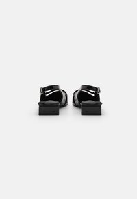Zwarte gepatenteerde leren sandalen met een lage blokhak, open achterkant, verstelbare enkelband en een gladde voering.
