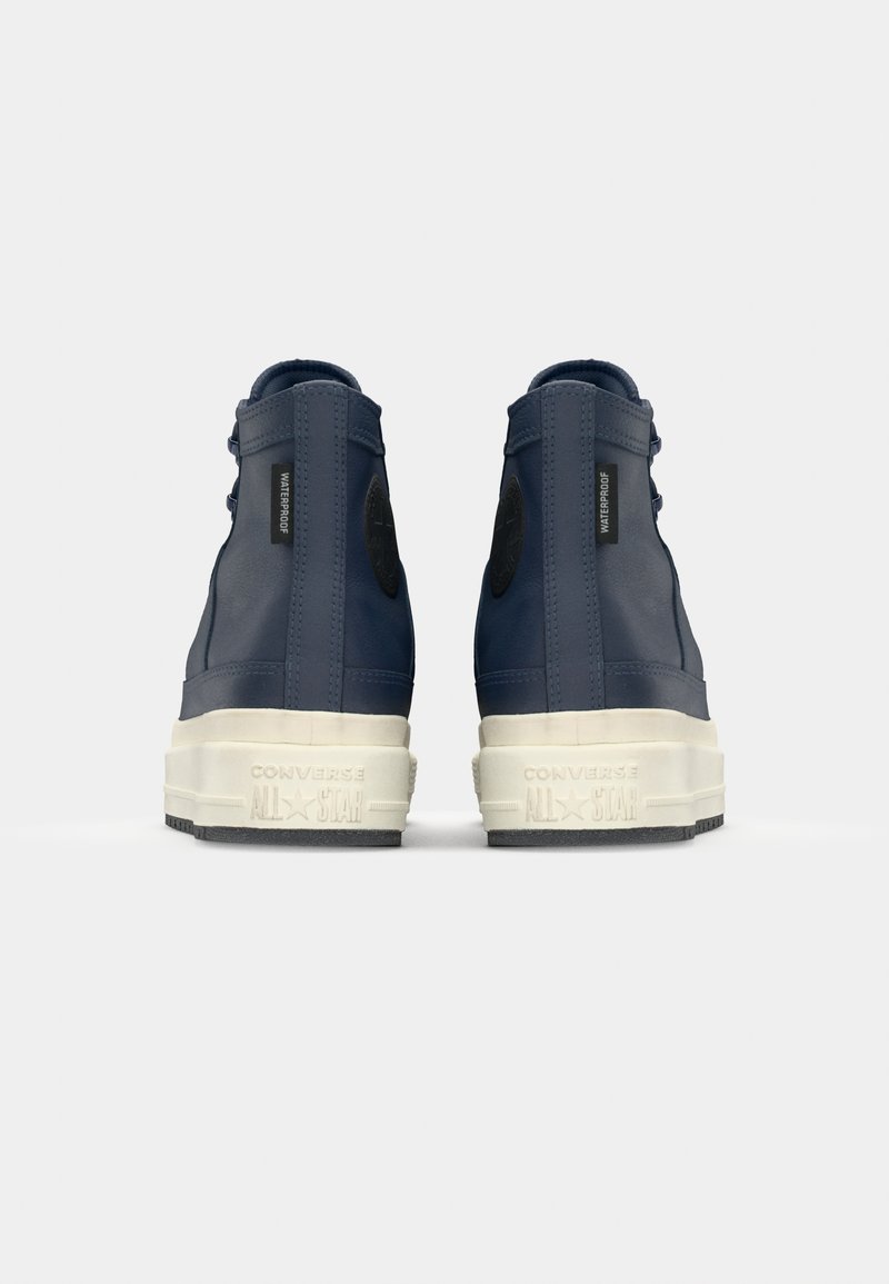 Marinblå vattentäta högtoppsneakers tillverkade av slät gummi med en vit gummisula, med en svart logotypapplikation och texturerade detaljer.