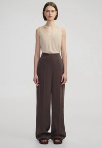 Krémový bezrukávový top s v�ýstřihem do V, který je spárován s volnými, tmavohnědými kalhotami s vysokým pasem, s plisováním a měkkou látkou. Černé sandály.