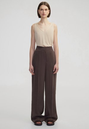 Top beige senza maniche con scollo a V abbinato a pantaloni larghi, marrone scuro, a vita alta con pieghe e tessuto morbido. Sandali neri.