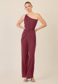 Jumpsuit bordeaux a spalla unica con dettaglio della vita intrecciato e design a gamba larga, realizzato in tessuto morbido. Finiture in argento sulla spalla.