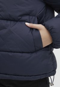 Námořnická prošívaná bunda s měkkou texturou, s boční kapsou a elastickým stahováním na lemu. Hřejivý, izolační design pro chladnější počasí.