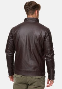 Chaqueta de cuero marrón con un alto cuello, detalles acolchados en los hombros y puños con cremallera. Acabado texturizado con un diseño ajustado.